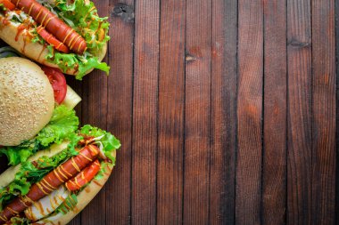 Sosisli sandviç ve hamburger ile peynir, et ve Yeşiller ahşap arka plan üzerinde. Üstten Görünüm. Boş alan.