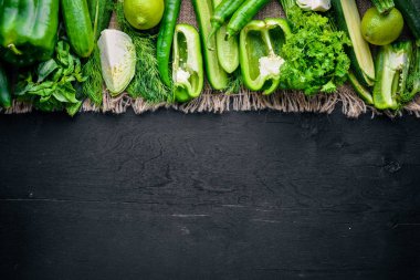 Yeşil sebzeler büyük bir set keten kumaş, ahşap zemin üzerinde ortaya koydu. Üstten Görünüm. Boş alan.