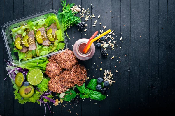 Yulaf ezmeli kurabiye ve sebze ile Dana ve yeşil salata. Sağlıklı bir diyet yemek. Öğle Yemeği boks. Siyah ahşap arka plan üzerinde. Üstten Görünüm. Metin için boş alan.