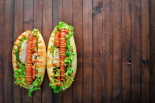 Perro caliente con salchicha a la parrilla, mostaza y ketchup, cebollas y verduras sobre fondo de madera. Vista superior. Espacio libre . — Foto de Stock
