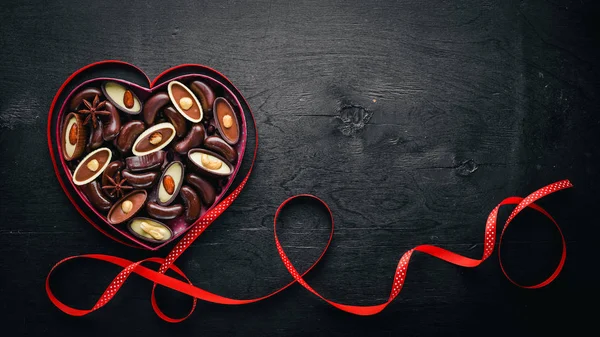 Chocolate box in the form of heart. On a black background Wooden. Top view. — Stock Photo, Image