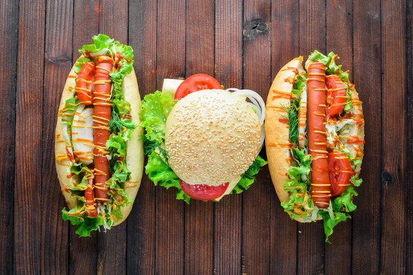 Perro caliente y hamburguesa con queso, carne y verduras sobre fondo de madera. Vista superior. Espacio libre . — Foto de Stock