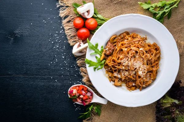 Kiraz domates, zeytin ve parmesan peyniri ile mantarlı makarna. İtalyan yemeği. Bir siyah ahşap yüzeye. Metniniz için boş alan. Üstten Görünüm.