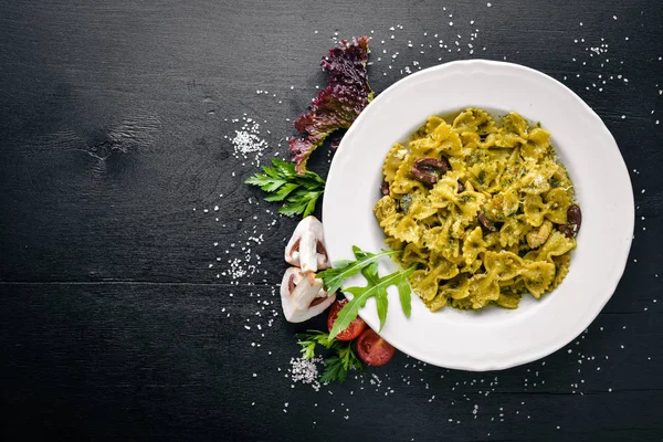 Pasta con espinacas, aceitunas y champiñones con queso parmesano. Comida italiana. Sobre una superficie de madera negra. Espacio libre para tu texto. Vista superior . — Foto de Stock