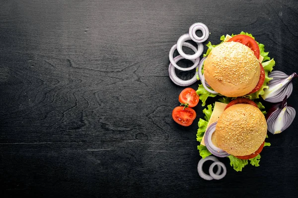 Hambúrguer com queijo, carne, tomate e cebola e ervas. Sobre fundo de madeira. Vista superior. Espaço livre . — Fotografia de Stock