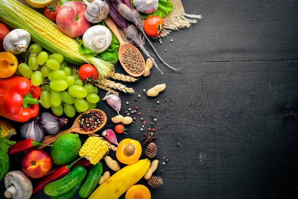 Çiğ sebze, meyve ve baharat bir siyah ahşap yüzey üzerinde büyük bir seçim. Metniniz için boş alan. Üstten Görünüm.