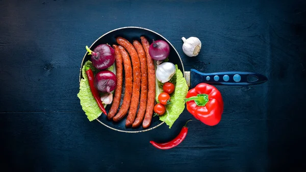 Taze sebze ile bir tavada ızgara sosis. Siyah yüzeyi ahşap. Üstten Görünüm.