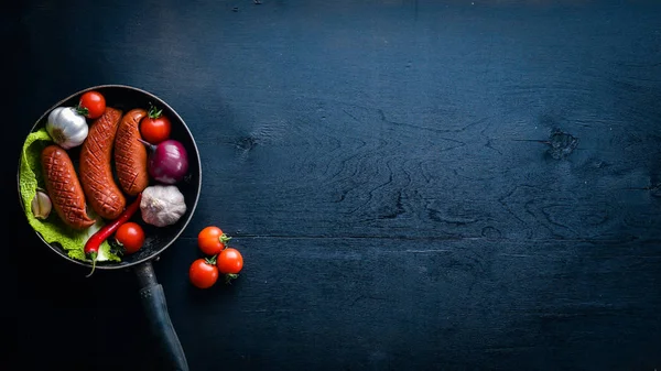 Taze sebze ile bir tavada ızgara sosis. Siyah yüzeyi ahşap. Üstten Görünüm.