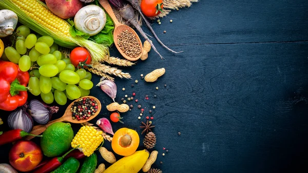 Çiğ sebze, meyve ve baharat bir siyah ahşap yüzey üzerinde büyük bir seçim. Metniniz için boş alan. Üstten Görünüm.