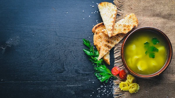 Broth from ravioli and herbs. Italian cuisine. On a wooden background. Top view. Free space for your text. — Stock Photo, Image