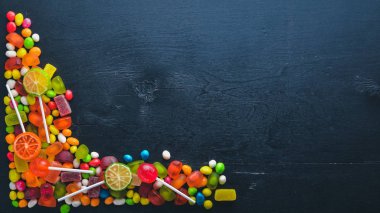 Renkli şeker, tatlılar ve lolipop. Siyah ahşap arka plan üzerinde. Üstten Görünüm. Boş alan.