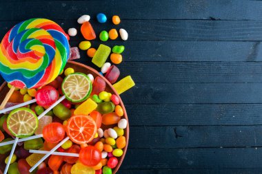 Renkli şeker, tatlılar ve lolipop. Siyah ahşap arka plan üzerinde. Üstten Görünüm. Boş alan.