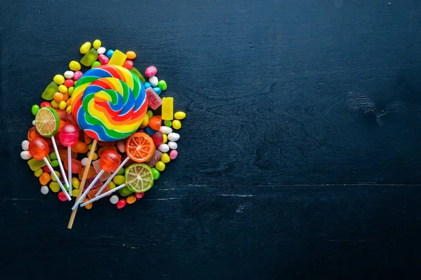 Caramelos de colores, dulces y piruletas. Sobre un fondo de madera negro. Vista superior. Espacio libre . — Foto de Stock