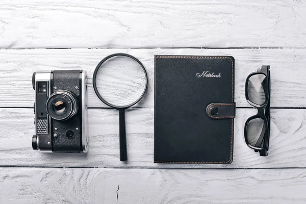 Irodai munkahelyét a fényképezőgép, a notebook, a szemlencse és a toll. A fa felületén. Felülnézet. Szabad hely a szöveg. — Stock Fotó