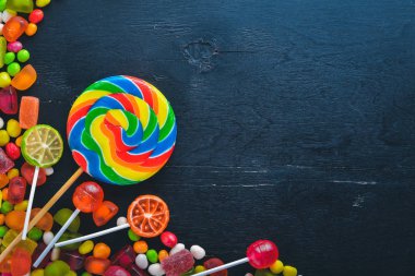 Renkli şeker, tatlılar ve lolipop. Siyah ahşap arka plan üzerinde. Üstten Görünüm. Boş alan.