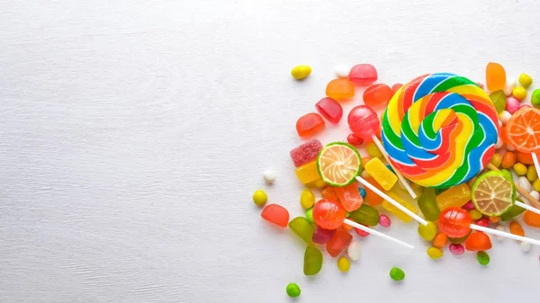 Caramelos de colores, dulces y piruletas. Sobre un fondo de madera blanca. Vista superior. Espacio libre . — Foto de Stock