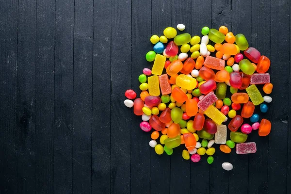 Colored candies, sweets and lollipops. On a black wooden background. Top view. Free space. — Stock Photo, Image