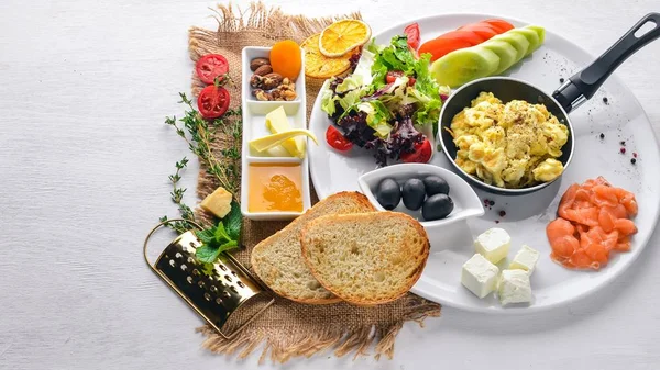 English breakfast. Fried eggs, salmon, olives, nuts, vegetables and dried fruit. Top view. Free space for text. On a wooden background.