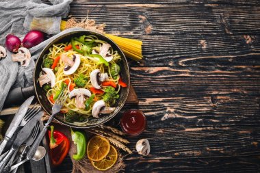 Bir tavada sebzeli erişte. Asya Mutfağı makarna. Üstten Görünüm. Boş alan. Ahşap bir arka plan üzerinde.;