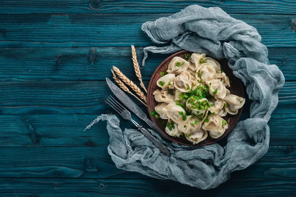 Tasty homemade meat dumplings of wholemeal flour or russian pelmeni sprinkled with fresh parsley on plate on wooden table,copy space, view from above — Stock Photo, Image