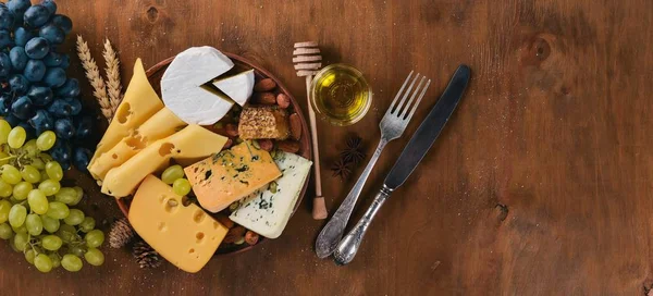 Uma garrafa de vinho e uma grande variedade de queijos, mel, nozes e especiarias, em uma mesa de madeira. Vista superior. Espaço livre para texto . — Fotografia de Stock