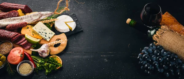Una botella de vino, quesos y salchichas tradicionales sobre un fondo de madera. Queso brie, queso azul, gorgonzola, fuete, salami. Espacio libre para texto. Vista superior . — Foto de Stock