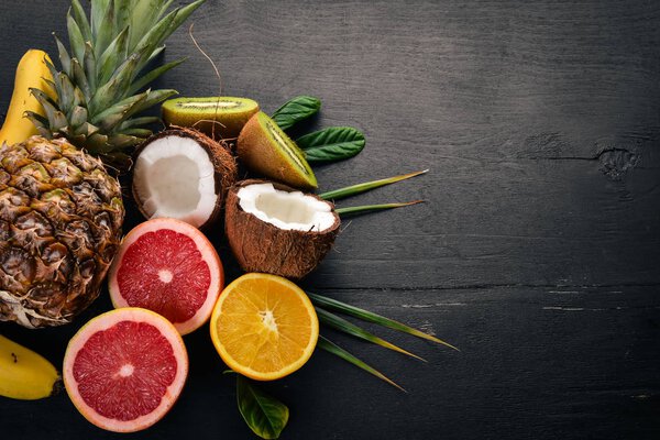 Свежие тропические фрукты. Ананас, кокос, киви, апельсин, гранат, грейпфрут. На деревянном фоне. Вид сверху. Свободное место для текста
.