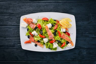 Somon salatası, beyaz peynir, salata yaprakları ve plaka üzerinde taze sebze. Ahşap bir arka plan üzerinde. Üstten Görünüm. Metin için boş alan.