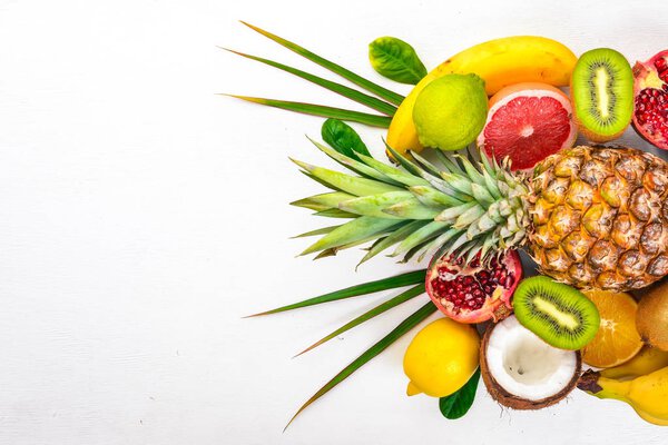 Fresh Tropical Fruits. Pineapple, coconut, kiwi, orange, pomegranate, grapefruit. On a wooden background. Top view. Free space for text.