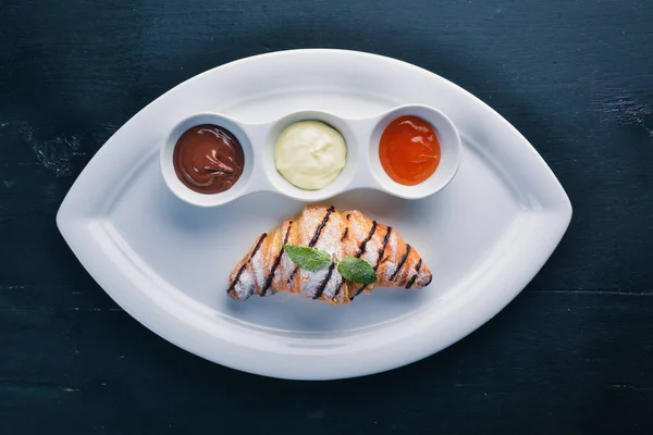 Croissant with sweet sauces. Chocolate, Vanilla and Peach. On a wooden background. Top view.