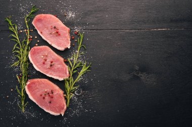 Çiğ et. Biberiye ve baharat siyah ahşap zemin sığır eti biftek. Üstten Görünüm. Metin için boş alan.