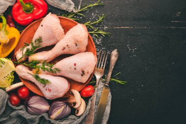 Taze sebze ve biberiye ve baharat siyah ahşap zemin ile çiğ tavuk budu. Üstten Görünüm. Metin için boş alan.