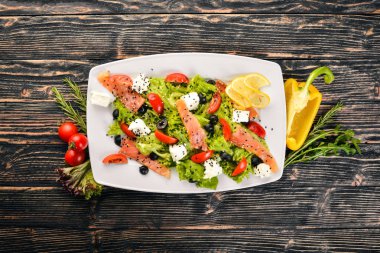 Somon salatası, beyaz peynir, salata yaprakları ve plaka üzerinde taze sebze. Ahşap bir arka plan üzerinde. Üstten Görünüm. Metin için boş alan.