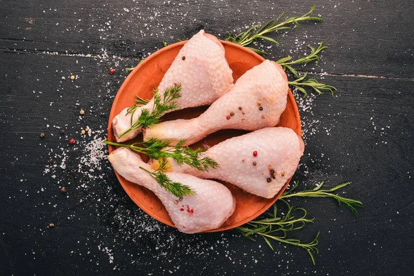 Raw chicken legs with rosemary and spices on a black wooden background. Top view. Free space for text.