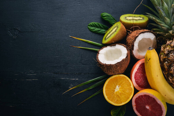 Свежие тропические фрукты. Ананас, кокос, киви, апельсин, гранат, грейпфрут. На деревянном фоне. Вид сверху. Свободное место для текста
.