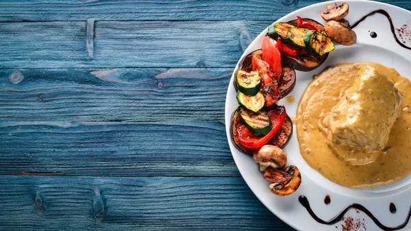 Meat steak with sauce and grilled vegetables. Steak Voronov. On a wooden background. Free space for your text. Top view.