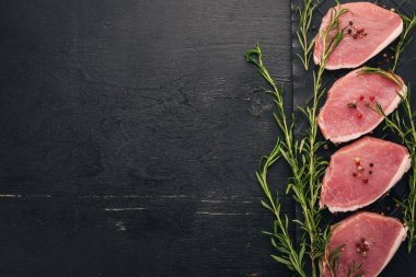 Çiğ et. Biberiye ve baharat siyah ahşap zemin sığır eti biftek. Üstten Görünüm. Metin için boş alan.