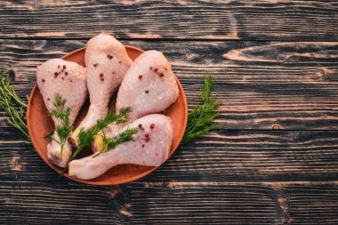 Biberiye ve baharat siyah ahşap zemin ile çiğ tavuk budu. Üstten Görünüm. Metin için boş alan.