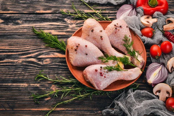 Raw chicken legs with fresh vegetables and rosemary and spices on a black wooden background. Top view. Free space for text.