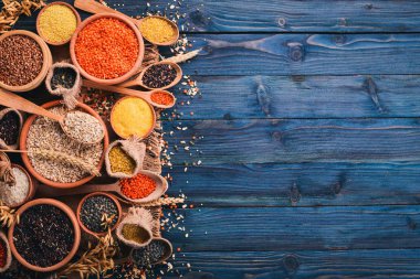 Kabuğu çıkarılmış tane ve tahıl kümesi. Buğday, mercimek, pirinç, darı, arpa, Mısır, siyah pirinç. Mavi ahşap arka plan üzerinde. Üstten Görünüm. Kopya alanı.