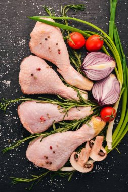 Taze sebze ve biberiye ve baharat siyah ahşap zemin ile çiğ tavuk budu. Üstten Görünüm. Metin için boş alan.