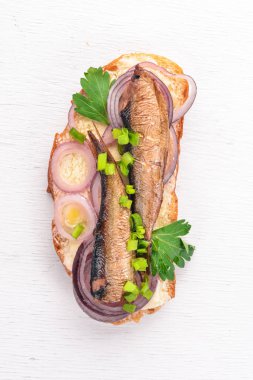 Sandwich with sprats, onions and parsley, on a wooden background. Top view. Copy space. clipart