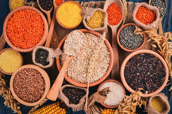 Set of Groats and Grains. Buckwheat, lentils, rice, millet, barley, corn, black rice. On a blue wooden  background. Top view. Copy space.