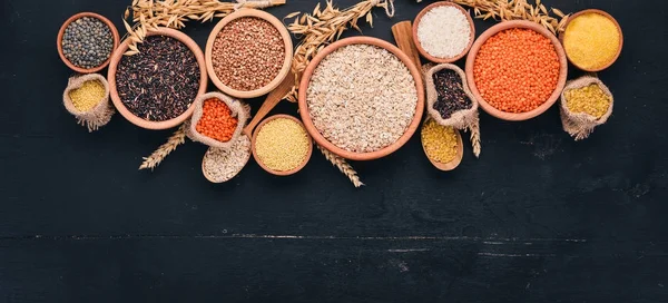 Set of Groats and Grains. Buckwheat, lentils, rice, millet, barley, corn, black rice. On a black background. Top view. Copy space.