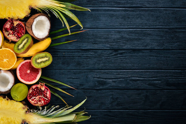 Fresh Tropical Fruits. Pineapple, coconut, kiwi, orange, pomegranate, grapefruit. On a wooden background. Top view. Free space for text.