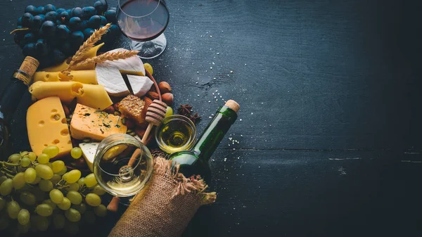 Assortment of cheeses, a bottle of wine, honey, nuts and spices, on a wooden table. Top view. Free space for text.