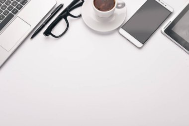 Beyaz Ofis Masası. Dizüstü bilgisayar, telefon, fincan kahve, gözlük, kalem, kalem. Beyaz bir arka plan üzerinde. Üstten Görünüm. Metin için boş alan.