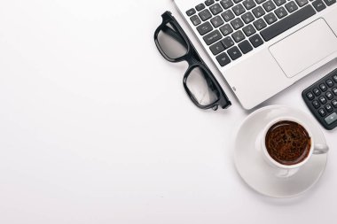 Beyaz Ofis Masası. Dizüstü bilgisayar, telefon, fincan kahve, gözlük, kalem, kalem. Beyaz bir arka plan üzerinde. Üstten Görünüm. Metin için boş alan.