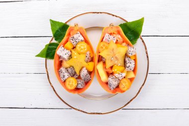 Tropikal meyve salatası servis yarım bir Papaya. Dragon meyve, rambutan, demirhindi, kaktüs meyve, avokado, mango. Ahşap bir arka plan üzerinde. Üstten Görünüm.