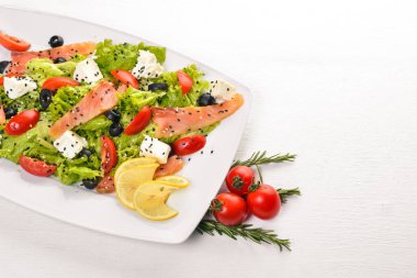 Somon salatası, beyaz peynir, salata yaprakları ve plaka üzerinde taze sebze. Ahşap bir arka plan üzerinde. Üstten Görünüm. Metin için boş alan.